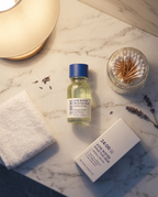 Flat lay of the drying lotion with its box, cotton buds and a folded towel on marble